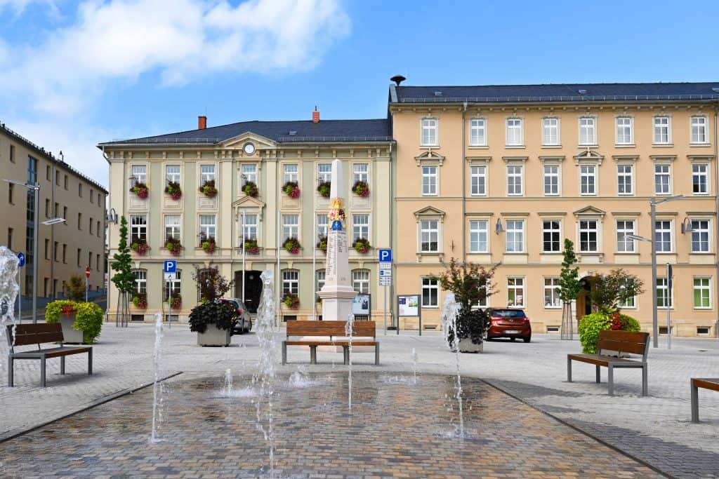 Platz mit Wasserspiel und Rathaus im Hintergrund im Sommer